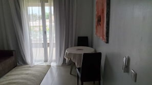 A room with a dining table, chairs, a sofa, and a sliding glass door leading to an outdoor area.