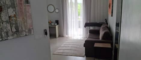 Una sala de estar con sofá, mesa de centro, alfombra, escritorio con silla y ventana con cortinas.