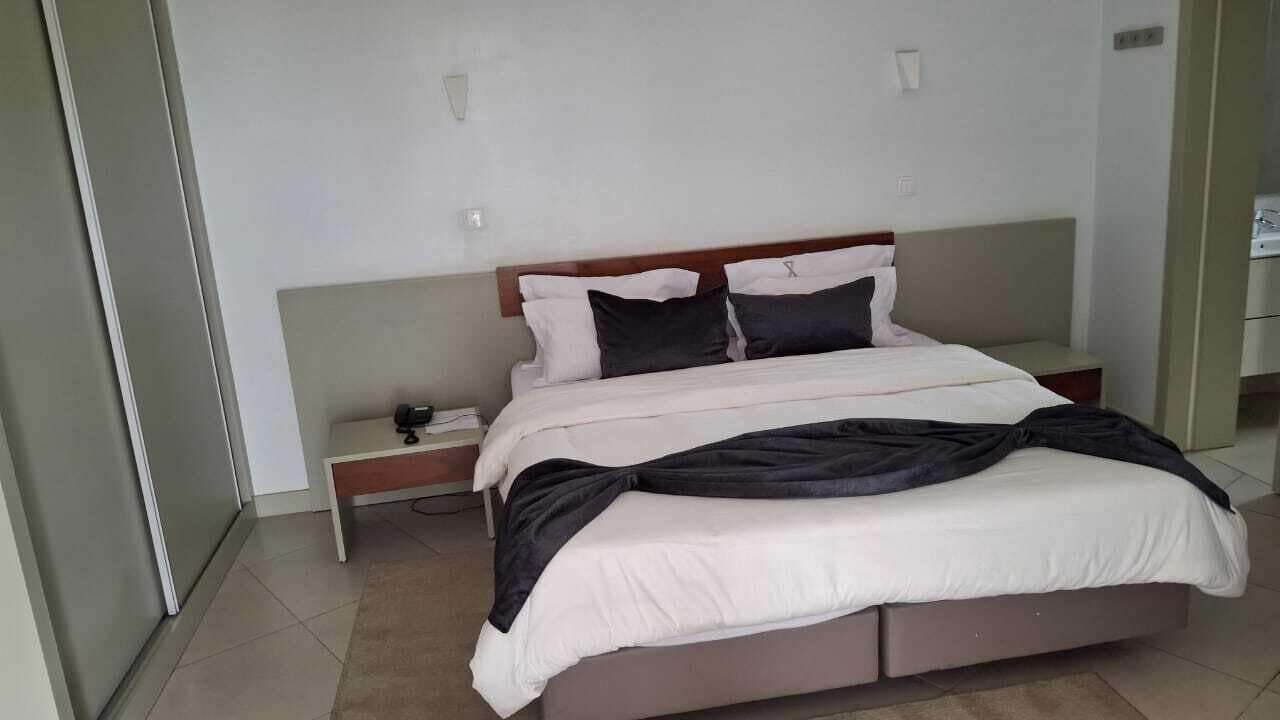 A bed with a wooden headboard, a bedside table, and a wall-mounted light fixture.