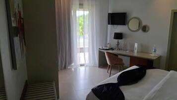 Quarto de hotel com cama, escrivaninha, cadeira, televisão e janela com cortinas.
