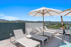 Eine Dachterrasse mit Liegestühlen und Sonnenschirmen mit Blick auf eine Stadtlandschaft und Hügel.