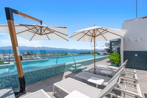 Un espace aménagé au bord de la piscine, avec des chaises longues et des parasols, une vue dégagée sur la mer et une piscine carrelée.