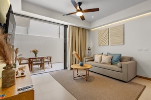 A modern living room with a ceiling fan, a sofa, a coffee table, and a dining area with chairs. - Coastal Condo with Rooftop Infinity Pool & Beach Club – La Cruz, Nayarit (Bahia de Banderas)