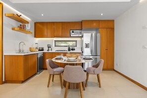 Une cuisine moderne avec des meubles en bois, des appareils électroménagers en acier inoxydable et un coin repas comprenant une table ronde et quatre chaises.