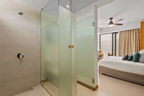 Ein modernes Hotelzimmer mit Glastrennwand, einem Bett mit Kissen, einem Deckenventilator und Blick ins Freie.