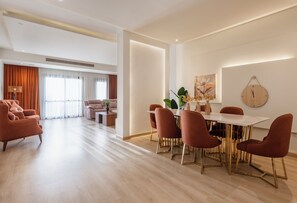 Uma sala de estar moderna com um sofá, uma mesa de jantar com cadeiras e uma grande janela com cortinas.