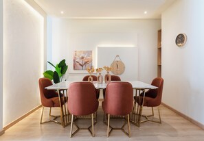 A dining area with a white table, six red chairs, and a wooden wall clock. - Premium 3BR Residence in Sodic Eastown, New Cairo /Sleeps 8 (Cairo Governorate)