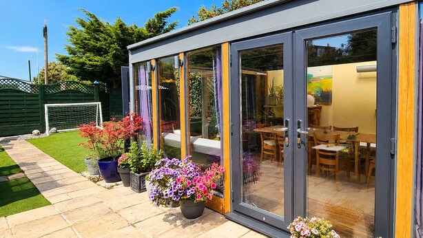 Ein modernes Haus mit Glastür, die zu einem Essbereich führt, umgeben von einem gepflegten Garten.