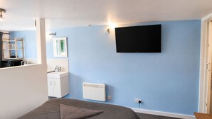 Ein Schlafzimmer mit einem Bett, einem an der Wand montierten Fernseher, einer Heizung und einem durch eine offene Tür einsehbaren Badezimmer.