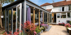 Ein modernes Haus mit großen Glasüren, einem Garten mit Kübelpflanzen und einer gefliesten Terrasse.