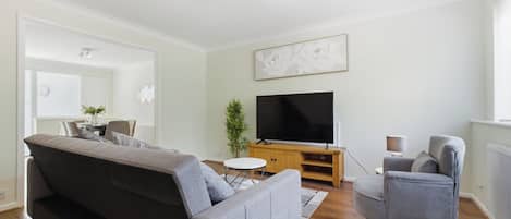 A modern living room with a grey sofa, a television on a wooden stand, a small round table, and a potted plant.