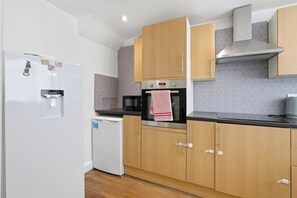 A modern kitchen with wooden cabinets, a built-in oven, a microwave, and a water dispenser. - Spacious 3-Bed House in Waltham Cross Sleeps 8 (Waltham Cross)