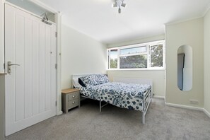 A bedroom with a single bed, a nightstand, a window with blinds, and a door with a handle. - Spacious 3-Bed House in Waltham Cross Sleeps 8 (Waltham Cross)