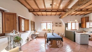 A rustic kitchen with wooden beams, a dining area with a table and chairs, and a view of the outside through a window. - Authentic Umbrian Escape with Pool & Olive Grove (Umbria)
