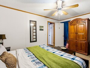 Ein Schlafzimmer mit Bett, Nachttisch, Schminktisch, Deckenventilator und einer Tür zu einem anderen Raum.