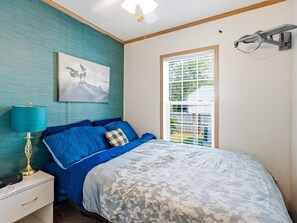 Un dormitorio con una cama, una mesita de noche, una lámpara, una ventana con persianas y un aplique de pared.