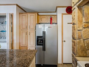 A kitchen with a stainless steel refrigerator, wooden cabinets, a granite countertop, and a stone accent wall. - Perdido Hideaway in Pensacola (Pensacola)