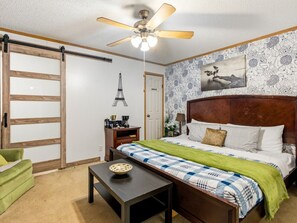 Een slaapkamer met een bed, bureau, stoel, plafondventilator en een deur.