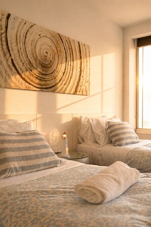 Een slaapkamer met een groot abstract schilderij, een bed met beddengoed met een patroon, een nachtkastje met een lamp en een raam met natuurlijk licht.