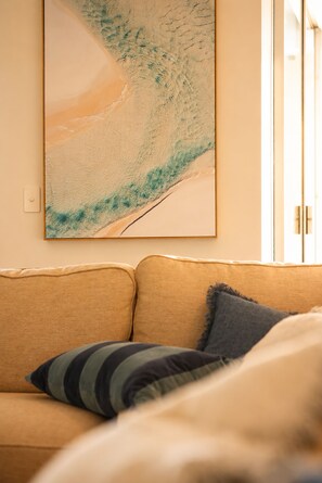 A room with a beige sofa, a framed abstract painting, and a window with blinds. - Luxury Suite| Surfers Paradise|Ocean Views (Surfers Paradise)