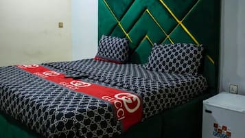A bed with a green upholstered headboard, patterned bedding, and pillows with a chain design.