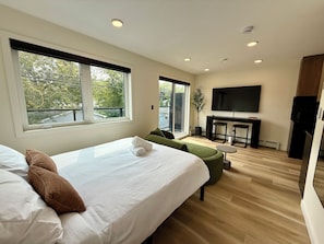 A modern hotel room with a large bed, a seating area, a television, and a view of the outdoors.