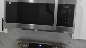 Um forno micro-ondas de aço inoxidável com visor digital e painel de controle, instalado acima de um forno embutido com relógio digital.