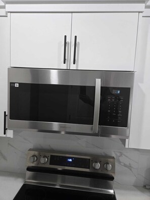 Eine Mikrowelle aus Edelstahl mit digitalem Display und Bedienfeld, oberhalb eines eingebauten Ofens mit digitaler Uhr.