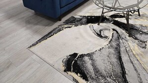 Uma sala de estar moderna com um sofá azul, uma mesa de centro de vidro e um tapete estampado.