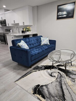 Ein modernes Wohnzimmer mit einem blauen Sofa, einem Glastisch und einem gemusterten Teppich.