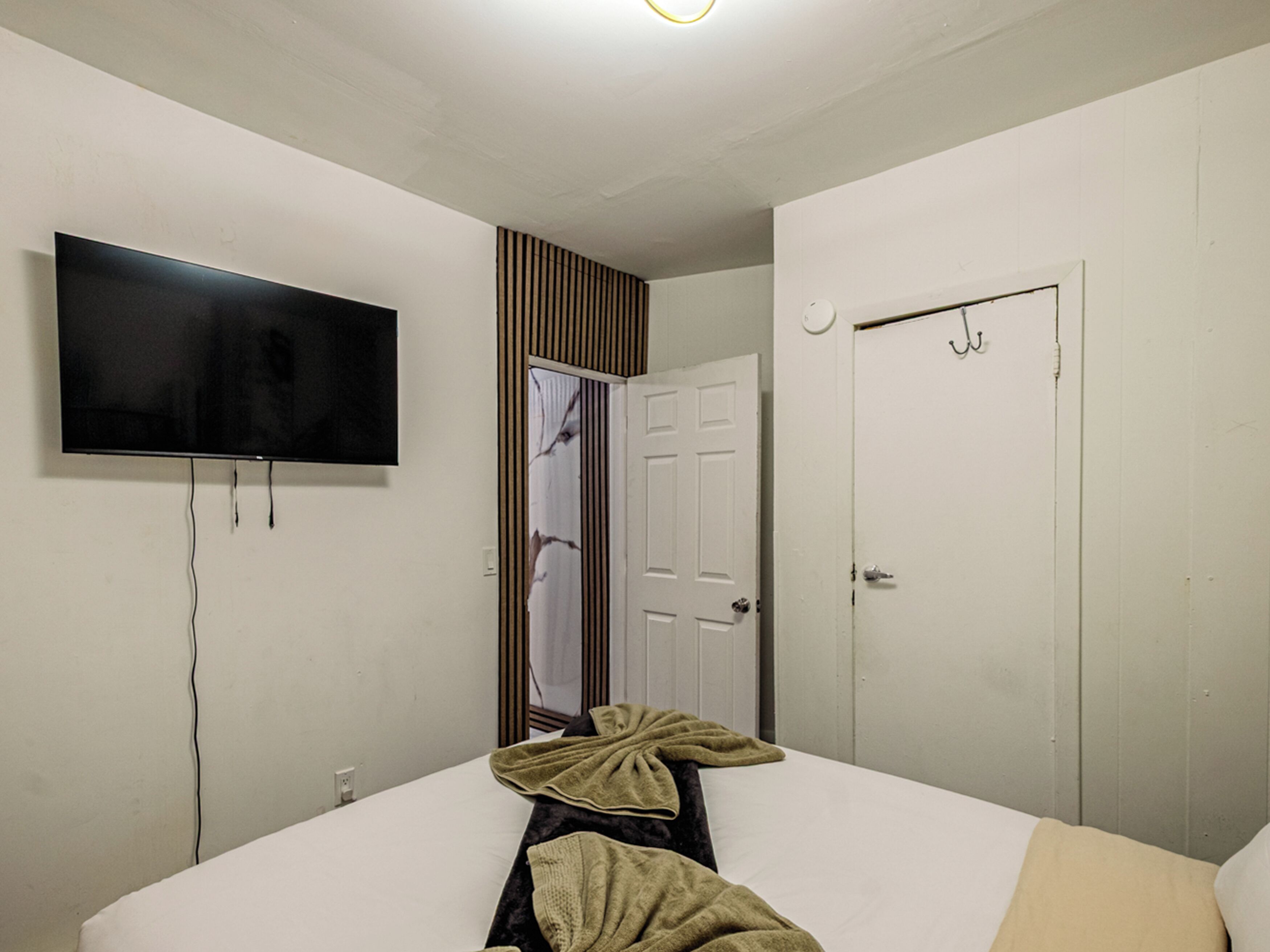 Une chambre d’hôtel avec un lit, un téléviseur fixé au mur, une porte et un miroir.