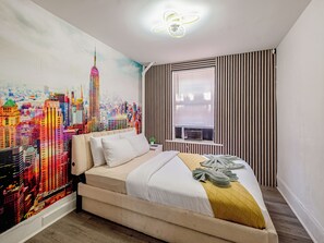 A hotel room with a cityscape mural, a bed with a white and yellow duvet, a window with blinds, and a ceiling fan. - Spacious 3BR Near Manhattan - Sleeps 7 (West New York)