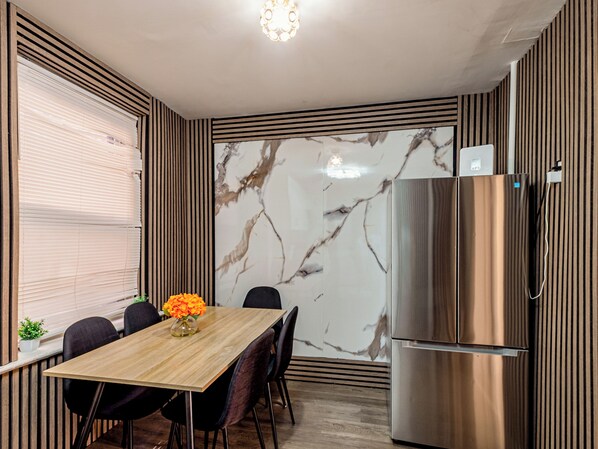 A modern kitchen with a marble backsplash, a stainless steel refrigerator, and a dining table with chairs.