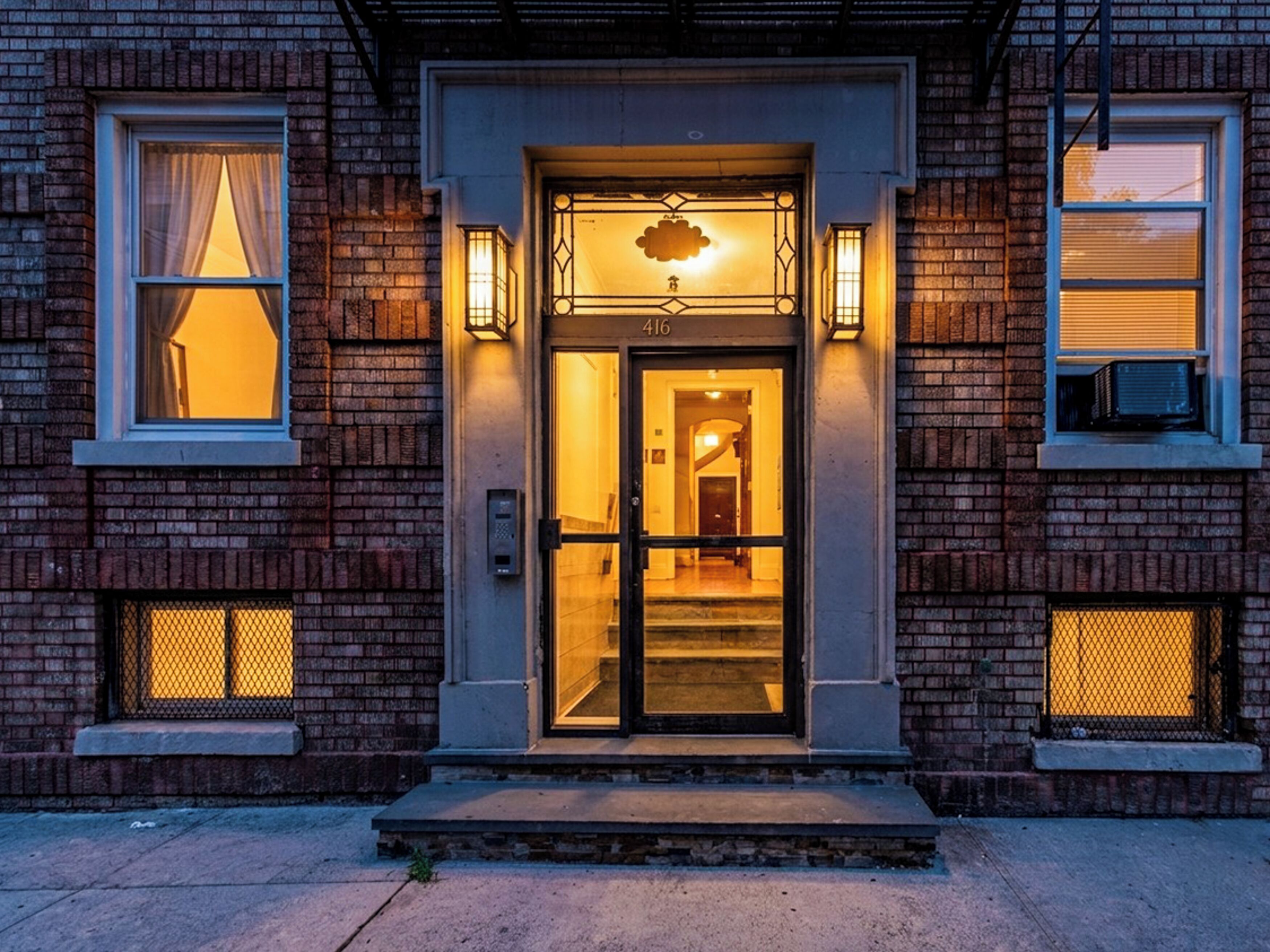A brick building with a glass door entrance, numbered 416, and two small windows with curtains.