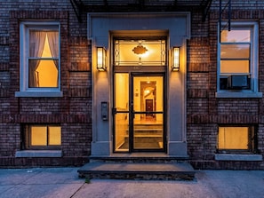 A brick building with a glass door entrance, numbered 416, and two small windows with curtains.