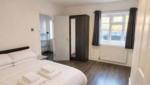 A hotel room with a bed, a wardrobe, a shelf unit, and a window with curtains. - Serviced Townhome: 4 bedroom, 3 bathroom+ garden (London)