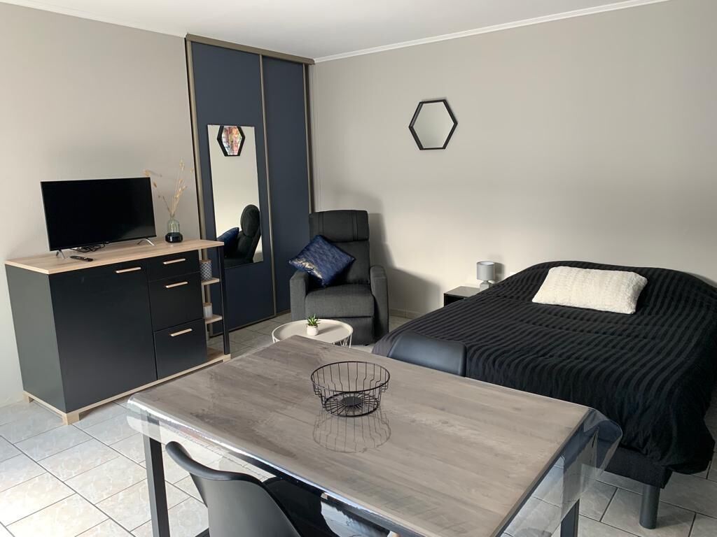 A modern hotel room with a bed, a desk with a computer, a chair, a small table, and a wardrobe.