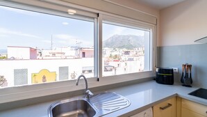 A kitchen with a large window, a stainless steel sink, and a view of a cityscape with buildings and mountains. - Cubo's Central Bright Marbella Apartment / urban / free wifi (Marbella)