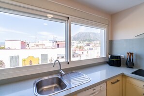A kitchen with a large window, a stainless steel sink, and a view of a cityscape with buildings and mountains. - Cubo's Central Bright Marbella Apartment / urban / free wifi (Marbella)