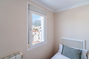 Ein Schlafzimmer mit einem Bett, einem Heizkörper und einem Fenster mit Blick auf Gebäude und Berge.