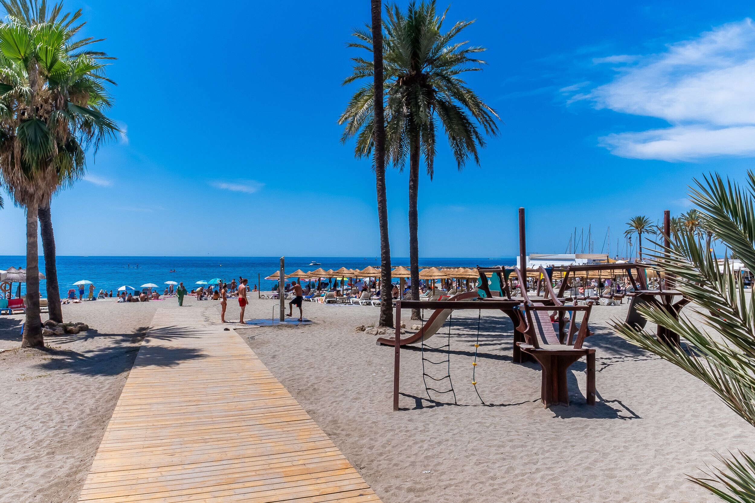 A beach with palm trees, a wooden walkway, and beach umbrellas.