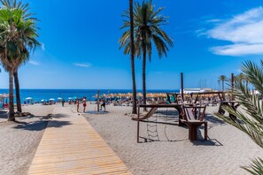 Ein Strand mit Palmen, einem Holzsteg und Strandsonnenschirmen.