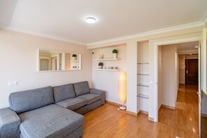 Ein modernes Wohnzimmer mit einem grauen Sofa, einem Spiegel, Regalen mit Dekoration und einer Stehlampe.