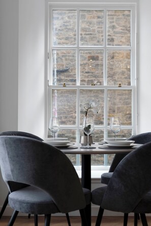 A dining area with a table set for two, two grey chairs, and a window with a stone wall view. - Modern Apartment in City Centre (Edinburgh)