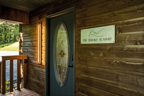 En stuga av trä med en dörr som har en dekorativ glaspanel och en skylt med texten ”The Smoky Summit”.