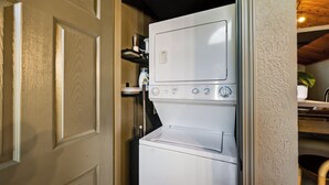 A compact, white laundry machine with a control panel, located in a small, enclosed space with a wooden door and a shelf above. - NEW Couples! VIEW, Barrel Sauna, Hot Tub, Fire Pit (Sevierville)