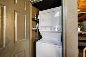 A compact, white laundry machine with a control panel, located in a small, enclosed space with a wooden door and a shelf above. - NEW Couples! VIEW, Barrel Sauna, Hot Tub, Fire Pit (Sevierville)