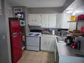 Uma cozinha compacta com armários brancos, uma geladeira vermelha, fogão, micro-ondas e cafeteira.