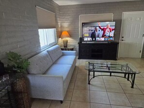 A living room with a sofa, a glass coffee table, a TV on a stand, a lamp, and a door. - Peaceful 2-bedroom condo with AC in sunny Tucson (Tucson)