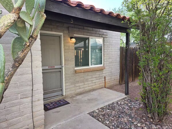 Uma casa com fachada de tijolos, porta de metal, janela com tela e um pequeno alpendre.